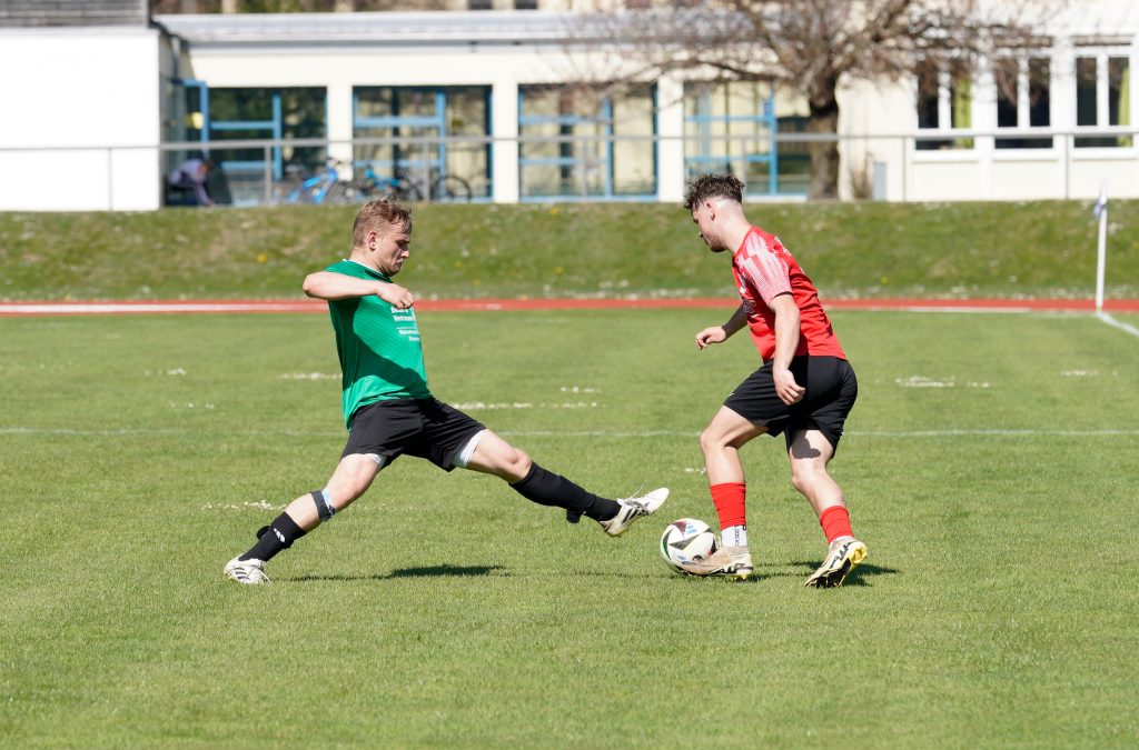 Foto zeigt einen Peißenberger Spieler mit dem linken Fuß den Ball spielend und von links einen Gegner mit gestecktem Bein kommend. Trifft aber nicht das Bein.