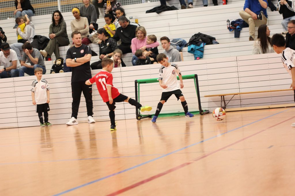 Fußball Turnier der Jahrgänge 2019 und 2020. Mehrere Spieler auf dem Feld, im Hintergrund die Tribüne mit Zuschauern.