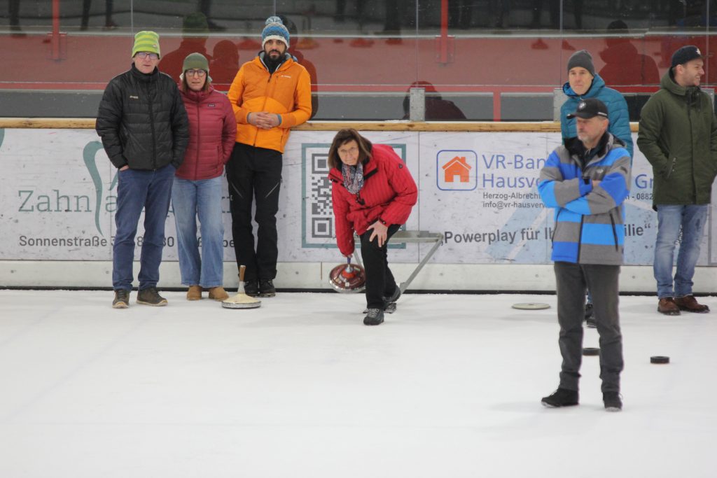 Foto zeigt eine Teilnehmerin in der Eishalle auf der Eisfläche, die gerade den Stock in der Hand lös läst. Um ihr rum ihre 3 Mannschaftskollegen. 