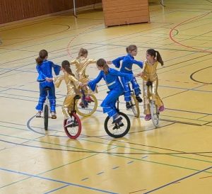 Bild zeigt eine Gruppe von 6 auf dem Einrad im Kreis fahrend und alle an der jeweiligen Hand haltend.