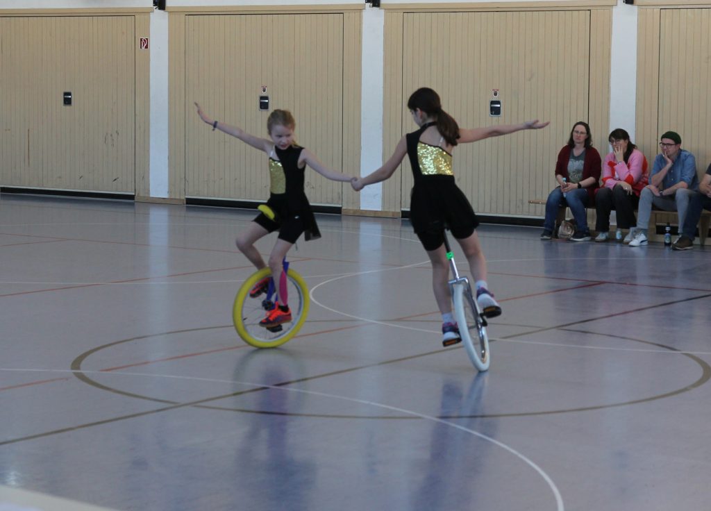 Foto zeigt in der Pause eine Vorführung von zwei Einrad Mädchen auf dem Einrad in der Halle, an der Hand haltend und im Kreis fahrend.