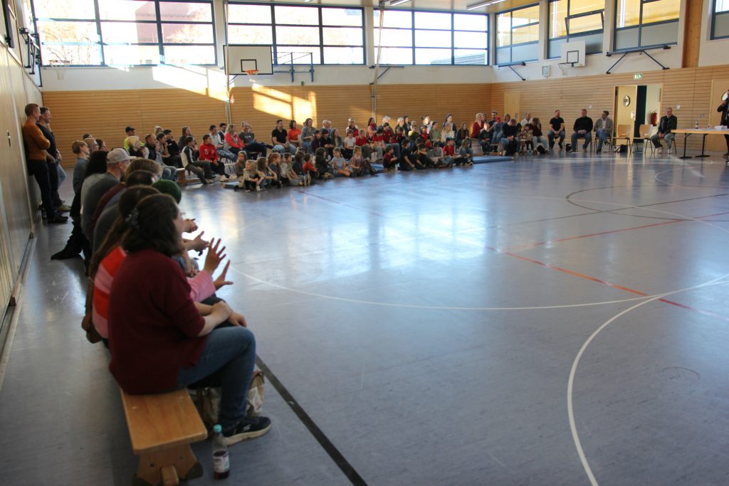 Foto zeigt die Teilnehmer in der Halle sitzend.