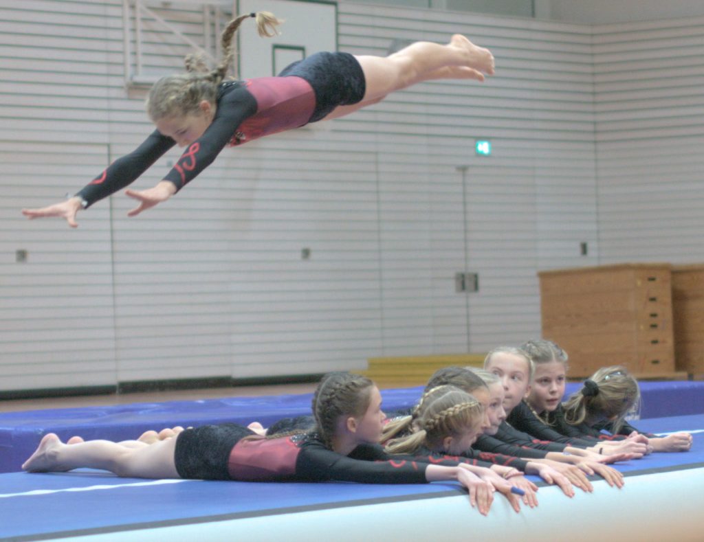 2 Foto vom Weihnachtsturnen in der Glückauf Turnhalle. Foto zeigt eine Aktive fliegend über 7 liegende.